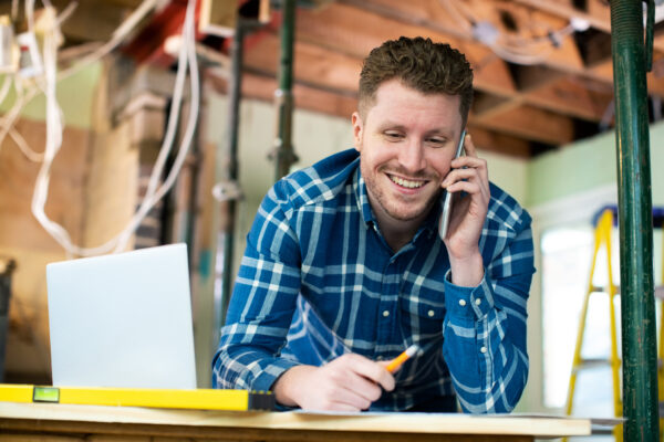 Smiling renovation contractor taking a phone call on an active job site — cost of delaying renovation