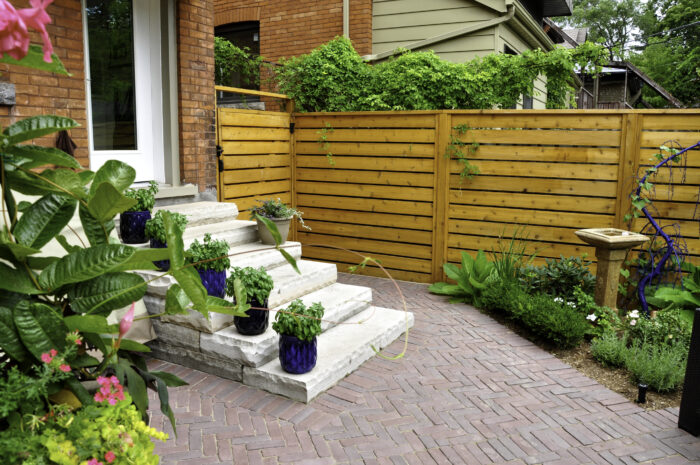 Backyard interlock patio with horizontal cedar privacy fence and potted herb garden on stone steps. outdoor living space ideas